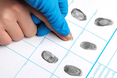 Technician assisting client with ink fingerprinting on FD-258 card for FBI background check.