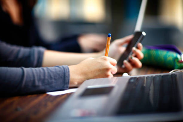 Person taking notes while checking phone with laptop on desk during apostille expedited service process