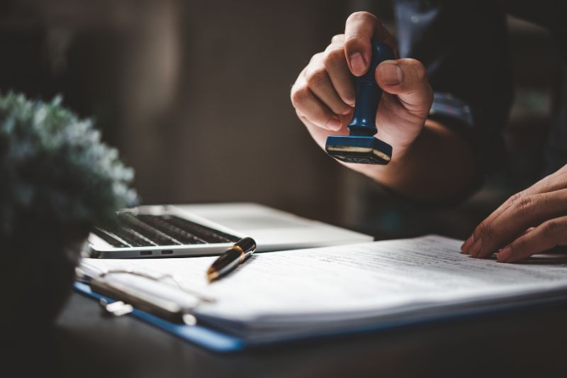 Person stamping official document for mobile Notary San Jose with pen and laptop on desk