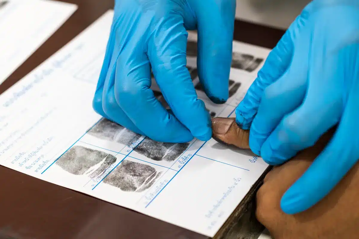 Gloved technician rolling an applicant's inked finger onto a fingerprint card